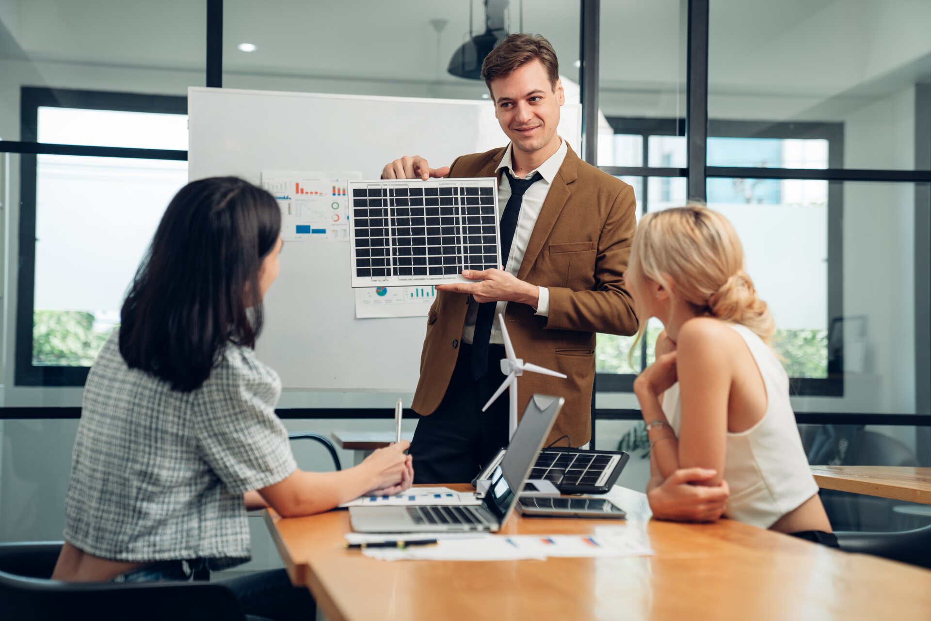 Ejecutivo presenta una fotografía con paneles solares a dos mujeres durante una reunión